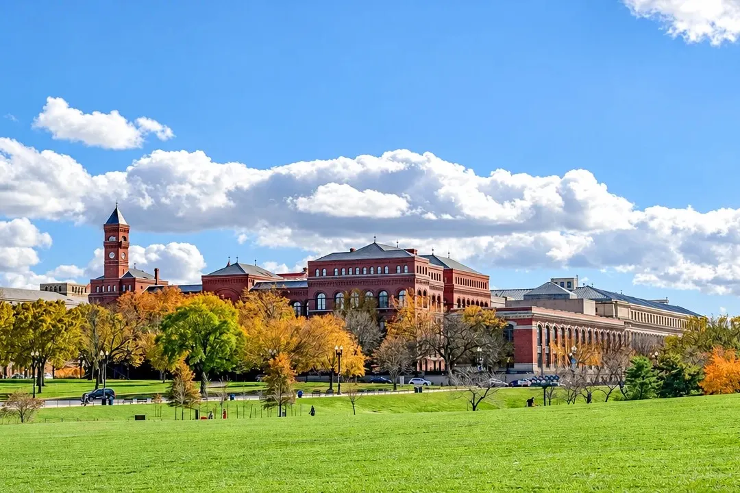 Red-brick university buildings across a wide green lawn on a sunny autumn day